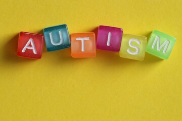 Obraz premium Word Autism made with colorful cubes on yellow background, top view. Space for text