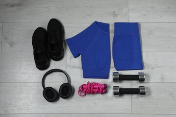 Stylish sportswear, black sneakers, dumbbells, skipping rope and headphones on wooden background,...
