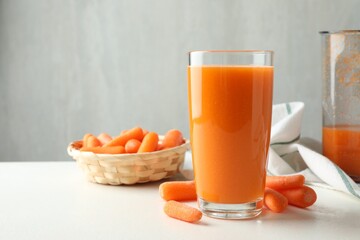 Fresh carrot juice in glass and vegetables on white table against gray background, space for text