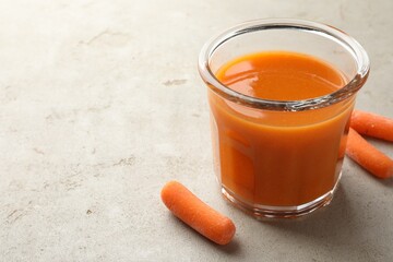 Fresh carrot juice in glass and vegetables on gray textured table, space for text