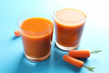 Fresh carrot smoothie in glasses and vegetables on light blue background, closeup