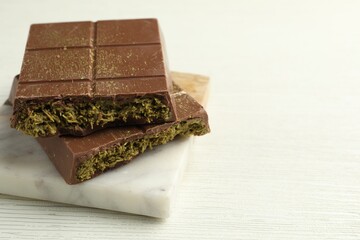 Pieces of tasty Dubai chocolate with pistachios and knafeh on white wooden table, closeup. Space for text