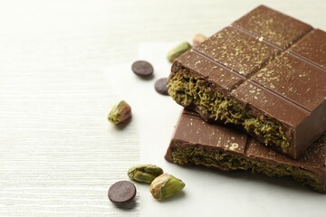 Pieces of tasty Dubai chocolate with pistachios, knafeh and cacao chips on white wooden table, closeup. Space for text