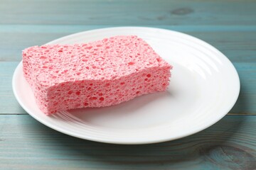 Pink sponge with foam and plate on light blue wooden table, closeup