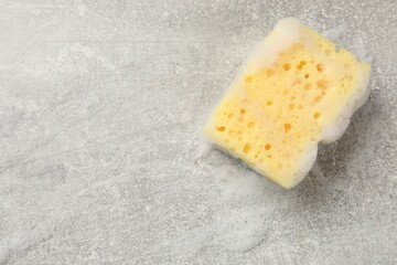 Yellow sponge with foam on gray textured table, top view. Space for text