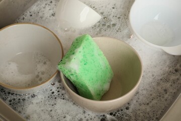 Green sponge, dishes and foam in sink, closeup