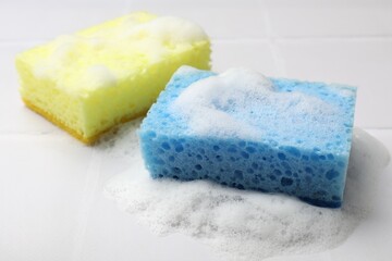Sponges and foam on white tiled table, closeup