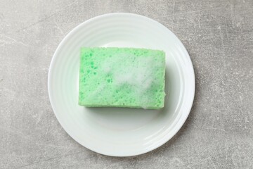 Sponge with foam and plate on light grey table, top view