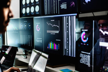 Stock market analysts monitoring real-time data, charts, and graphs on computer screens in a dark room. Financial investment and technology concept