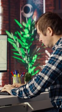 Man in home office looking at UI on PC screen, typing and executing programming code. Coding application UI used by IT developer writing and testing code in modern workspace, camera B