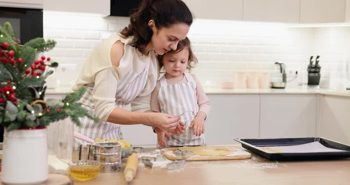 mother and little child daughter cut out various shapes of Christmas cookies in kitchen.