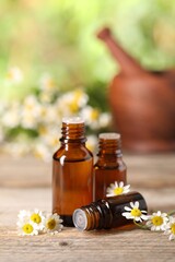 Bottles of essential oil and chamomile flowers on wooden table