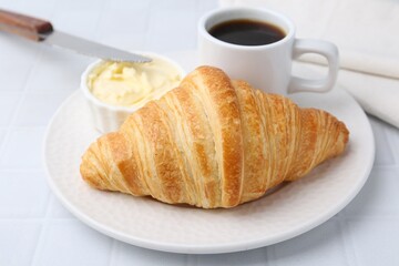 Tasty fresh croissant served with butter and cup of coffee on white tiled table, closeup