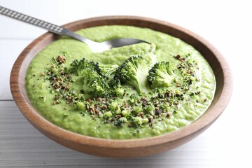 Delicious broccoli cream soup and spoon in bowl on white wooden table, closeup
