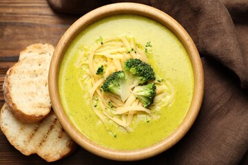Delicious broccoli cream soup in bowl and croutons on wooden table, flat lay