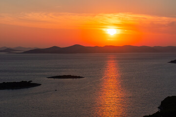 Stunning sunset over calm sea with vivid orange and red hues and silhouettes of small islands in the distance. Concept of peaceful nature scenery, tranquility, and breathtaking coastal views at dusk.