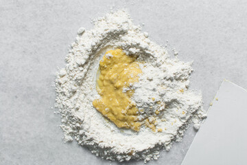 Overhead view of flour and egg being mixed on a white countertop, top view pasta dough being kneaded on a white granite countertop, process of making pasta and egg noodles