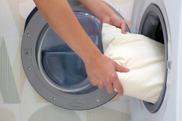 Man's hand holds a pillow and puts it in the washing machine.