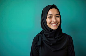 Woman wearing hijab smiles warmly at camera. Positive female portrait against vibrant teal background. Happy person enjoying moment. Image suitable for diverse topics as culture, faith, community.