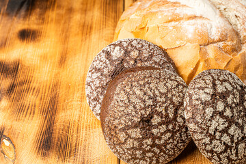 Round wheat bread and small rye bread rolls on a wooden background. Space for text. High quality photo