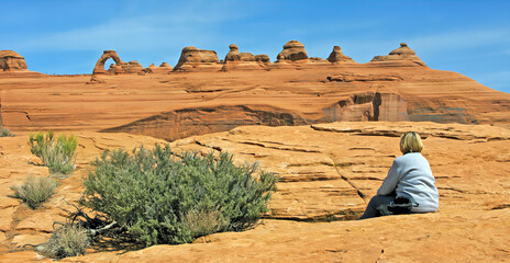 Delicate Arch, Utah Archs National park - Woman admires the view from a lower and distant view