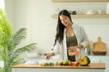 Beautiful young woman packing fresh vegetables into plastic container for freezing. Food storage.