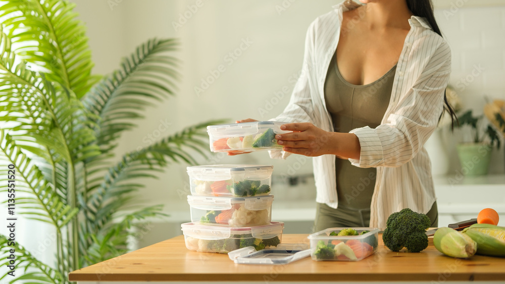 Wall mural Attractive woman arranging her meal prep containers on the kitchen counter, ready for a week of healthy eating. Healthy lifestyle and nutrition concept.