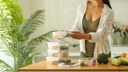 Attractive woman arranging her meal prep containers on the kitchen counter, ready for a week of...