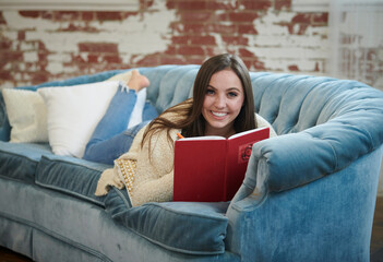 Adorable young brunette woman lays on vintage couch with journal