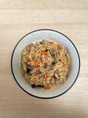 A bowl of rice with mushroom, chicken, and carrot.