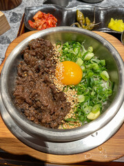 A bowl of beef, egg, green onion on rice.