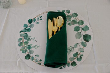 Gold silverware wrapped in green napkin on leaf decor placemat.