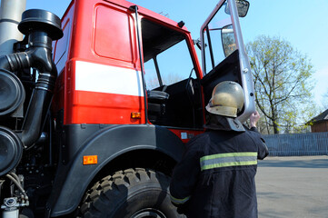 Fototapeta premium Fireman in protective costume get in cabin of a firetruck. Rescue team training of firefighting