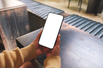 Mockup image of a woman holding and using mobile phone with blank desktop in cafe