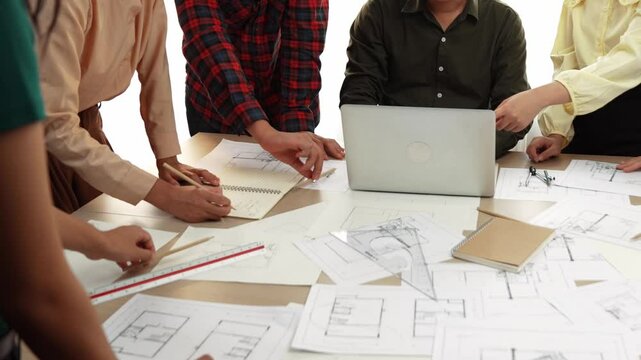 Architect and safety engineer discussion about building blueprint displaying on laptop on table with architectural document and wooden block scatter around at modern office. Closeup. Delineation.