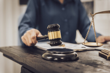 Close-up of an Asian female lawyer sitting at her desk in a law office. A wooden hammer and brass scales symbolize justice. She demonstrates expertise in the legal and justice process