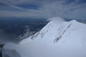 A stunning rock formation covered in snow, set against a clear blue sky with fluffy clouds in the background, creating a peaceful and breathtaking mountain landscape.
