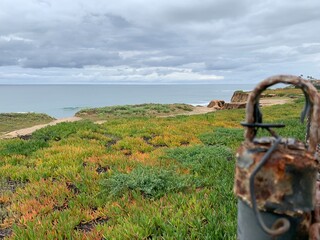 A view of the ocean and coastal bluffs through the rusted metal loop of a fence post.