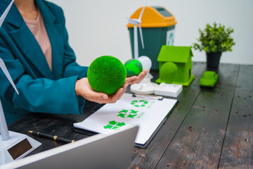 A businesswoman sits at a desk discussing the Earth, environment, renewable energy, and sustainability, with a power sled, trash can, and wind turbine symbolizing eco-friendly and green initiatives