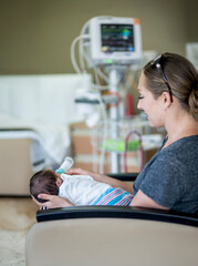 Young mother feeding her newborn baby boy in a hospital room. Side view of a woman giving her child a bottle of baby formula.