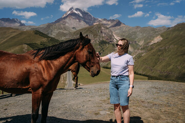 A girl strokes a brown horse against the background of Mount Kazbek in Georgia. Portrait of a girl...