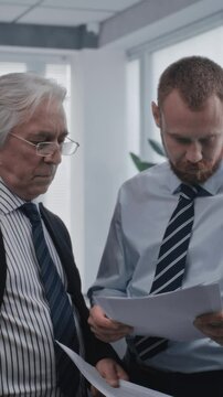 Two employees of international corporation with serious focused expression talking about business strategy and analyze financial reports on papers. Work in modern office of stock exchange company.