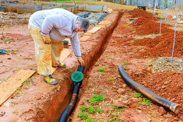 Gardener is carefully placing drainage pipe into trench to manage water flow efficiently while cultivating soil.