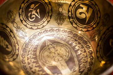A close-up view of an intricately designed Tibetan singing bowl featuring sacred symbols, Om patterns, and a detailed depiction of Avalokiteshvara, symbolizing compassion and spirituality