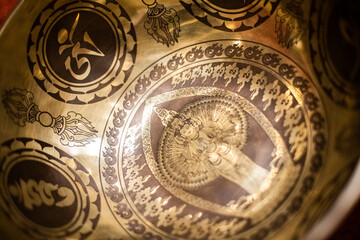 A beautifully engraved Tibetan singing bowl with Om symbols, sacred patterns, and a detailed Avalokiteshvara design, representing spiritual harmony and tranquility in a golden finish