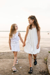 Two young girls are walking on beach, holding hands. The scene is peaceful and serene