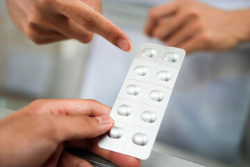 Image of a pharmacist advising a patient on the dosage of antihistamines at a pharmacy counter,...
