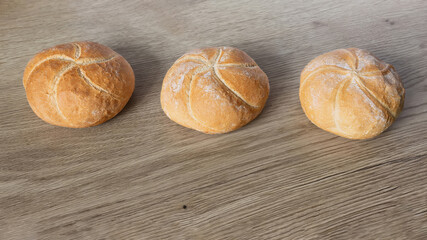 Three freshly baked kaiser burger buns neatly arranged on a wooden oak surface