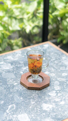 A glass of colorful two-tone drink, possibly a cocktail or refreshing beverage, sits on a textured table, outdoors. The drink has two distinct layers of color, a purple top and an orange bottom