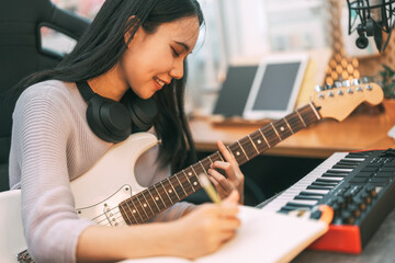 Young asian woman composer playing guitar music with digital technology at home studio